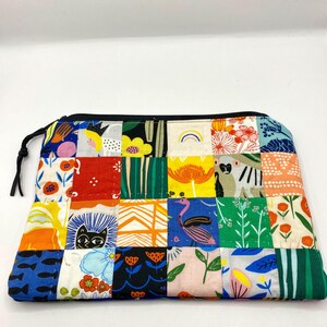 May include: A colorful patchwork zippered pouch featuring a variety of whimsical patterns. The design includes squares with floral, animal, and abstract motifs in shades of blue, red, orange, and green. The pouch has a black zipper and a black cord pull.