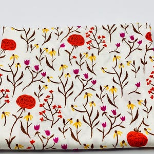 May include: White fabric with a repeating floral pattern. The design features red roses, yellow and purple wildflowers, and small red berries on brown stems. The fabric is folded, showing the pattern's repeat.