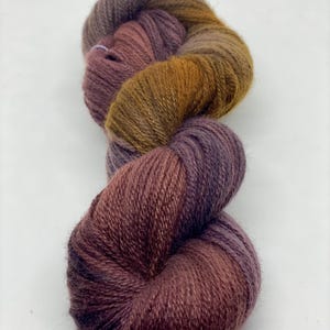 May include: A skein of yarn in shades of purple, brown, and orange. The yarn is soft and fluffy, and it is perfect for knitting or crocheting.