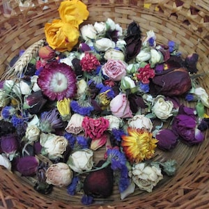 Könnte beinhalten: Ein geflochtener Weidenkorb gefüllt mit einer Vielzahl getrockneter Blumen, darunter gelbe, rosa, weiße und dunkelviolette Rosenknospen, leuchtend magentafarbene Strohblumen, blaue Kornblumen und ein einzelner Weizenhalm, locker angeordnet.