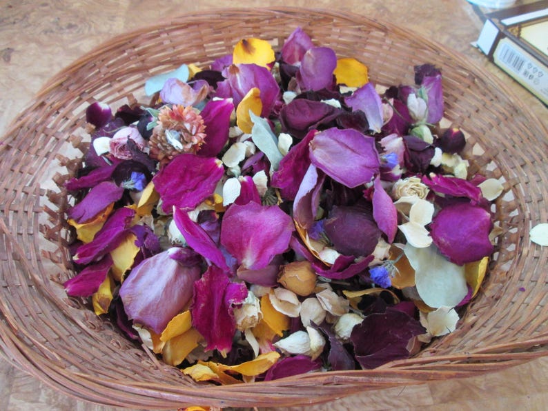 Puede incluir: Una cesta redonda de mimbre llena de p&eacute;talos de flores secas. Los p&eacute;talos son de color p&uacute;rpura, amarillo y blanco. La cesta est&aacute; hecha de material tejido de color marr&oacute;n claro.
