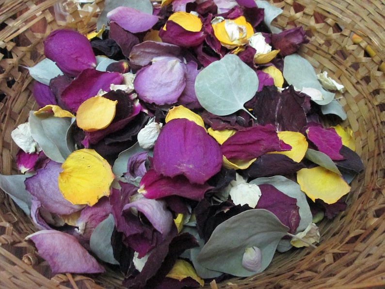 Puede incluir: Una cesta de mimbre llena de p&eacute;talos y hojas de flores secas. Los p&eacute;talos son de color p&uacute;rpura, amarillo y blanco, con algunas hojas de color verde gris&aacute;ceo. La cesta est&aacute; hecha de material tejido marr&oacute;n claro.