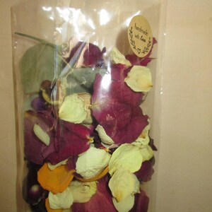 Puede incluir: Una bolsa transparente llena de p&eacute;talos de rosa secos en tonos burdeos, crema y amarillo. Una peque&ntilde;a pegatina ovalada con las palabras "handmade with love" est&aacute; adherida a la bolsa. Los p&eacute;talos parecen ser una mezcla de diferentes tipos de rosas.