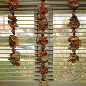 May include: Three vertical hanging garlands made of dried orange slices, green eucalyptus leaves, and small brown wooden beads strung together on natural twine. Each garland features alternating layers of citrus fruit and foliage.