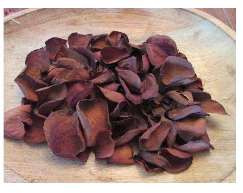 Puede incluir: Un mont&oacute;n de p&eacute;talos de rosa secos, de color burdeos, en un cuenco de madera marr&oacute;n claro. Los p&eacute;talos muestran una superficie texturizada con diversos tonos burdeos y marr&oacute;n. Los p&eacute;talos est&aacute;n dispuestos de forma informal, dando un aspecto natural y org&aacute;nico.