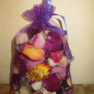 Puede incluir: Un saquito de malla morada lleno de flores y p&eacute;talos secos en tonos rosa, morado, naranja y blanco. El saquito est&aacute; atado con una cinta morada, creando un art&iacute;culo decorativo y arom&aacute;tico. Las flores parecen ser una mezcla de rosas y otros productos bot&aacute;nicos secos.