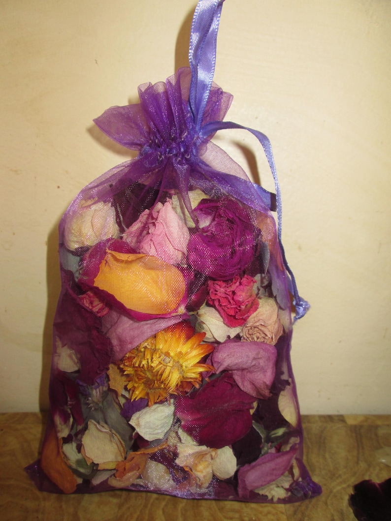 Puede incluir: Un saquito de malla morada lleno de flores y p&eacute;talos secos en tonos rosa, morado, naranja y blanco. El saquito est&aacute; atado con una cinta morada, creando un art&iacute;culo decorativo y arom&aacute;tico. Las flores parecen ser una mezcla de rosas y otros productos bot&aacute;nicos secos.