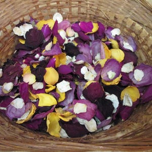 Puede incluir: Una cesta de mimbre llena de p&eacute;talos de rosa coloridos. Los p&eacute;talos son una mezcla de morado oscuro, amarillo, blanco y morado claro. La cesta est&aacute; hecha de material tejido marr&oacute;n claro.