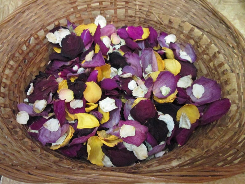 Puede incluir: Una cesta de mimbre llena de p&eacute;talos de rosa coloridos. Los p&eacute;talos son una mezcla de morado oscuro, amarillo, blanco y morado claro. La cesta est&aacute; hecha de material tejido marr&oacute;n claro.