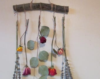 May include: A rustic wall hanging made from a branch with dried flowers and eucalyptus leaves hanging from it. The flowers are red, pink, yellow, and purple.