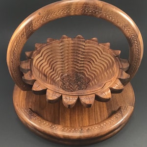 May include: A wooden fruit bowl with a carved sunflower design and a handle. The bowl is made of natural wood and has a rustic look.