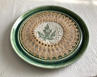 Green tray with woven cane bottom in a circular pattern and a medallion with a leaf and white beads.  12x12x1 inches
