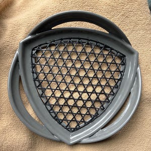 May include: A gray, triangular-shaped kitchen utensil with a black crisscross pattern in the center. The utensil has a handle and a curved edge. The item is likely used for straining or draining food items.