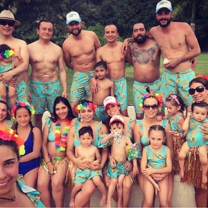 May include: A group of people wearing pineapple-themed swimsuits and accessories. Some are wearing leis, hats, and headbands. There are adults and children in the photo.