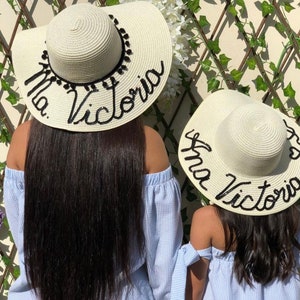 May include: Two white straw sun hats with black trim and the names "Ana Victoria" and "Mia Victoria" embroidered on them.