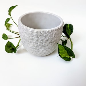 Op de afbeelding: Witte keramische pot met een geometrisch patroon. De pot is leeg en heeft een afgeronde vorm.