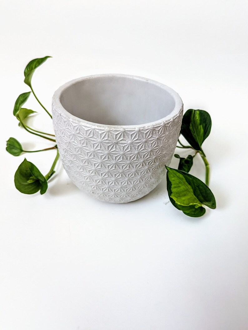 Op de afbeelding: Witte keramische pot met een geometrisch patroon. De pot is leeg en heeft een afgeronde vorm.