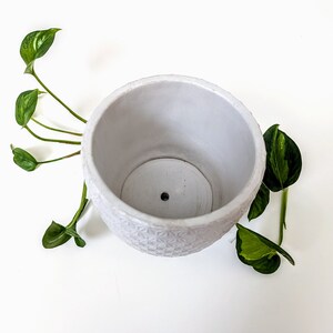 Op de afbeelding: Witte keramische pot met een geometrisch patroon. De pot heeft een drainagegat in de bodem.