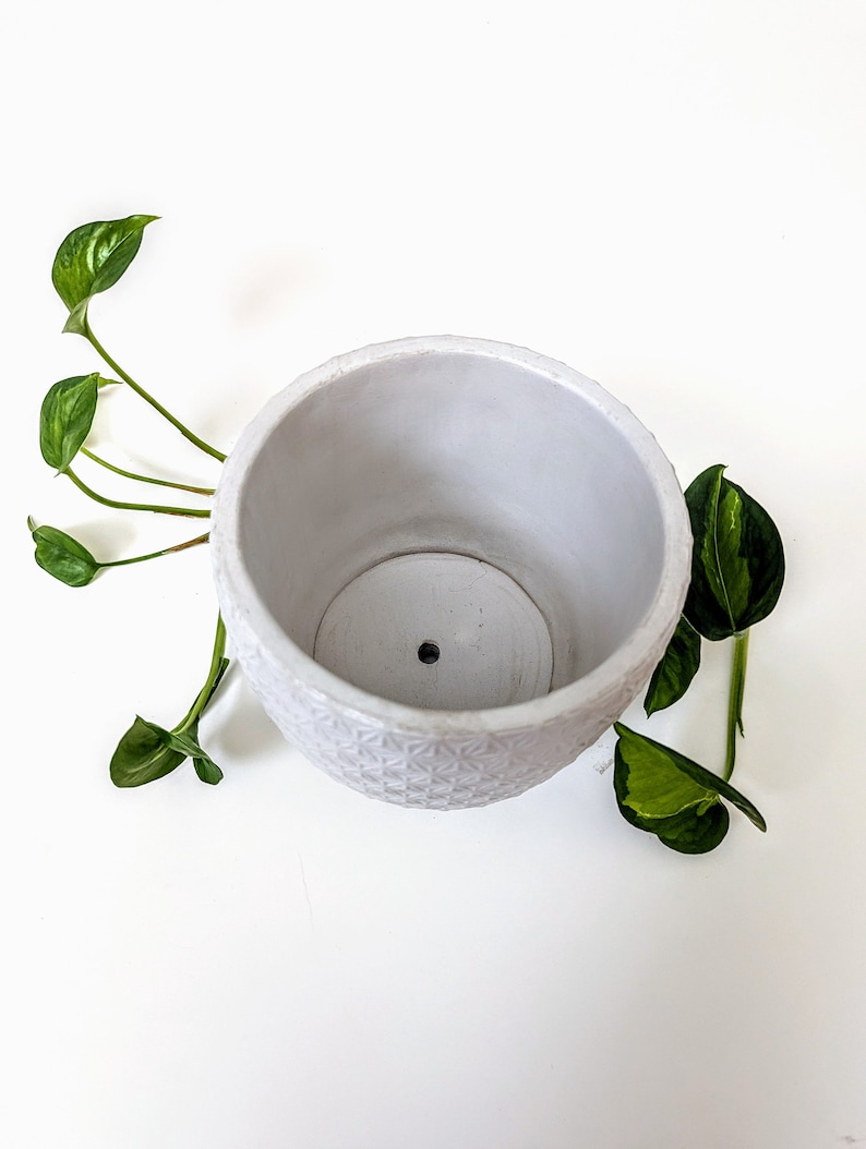 Op de afbeelding: Witte keramische pot met een geometrisch patroon. De pot heeft een drainagegat in de bodem.