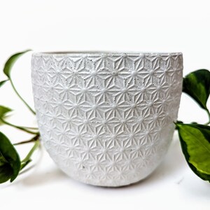 Op de afbeelding: Witte keramische plantenpot met een geometrisch stervormig patroon. De pot is rond en heeft een brede opening.