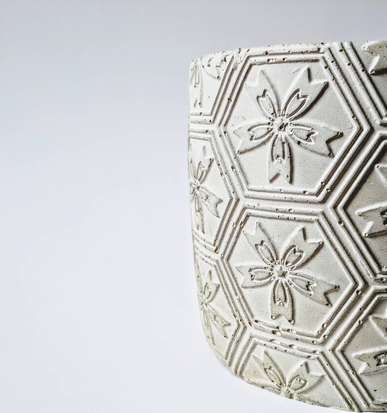 Puede incluir: Maceta de cer&aacute;mica blanca con un patr&oacute;n hexagonal y dise&ntilde;os de flores en relieve.