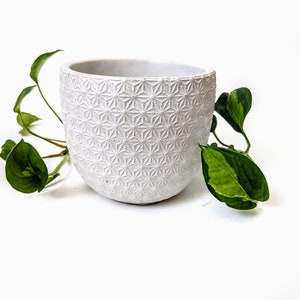 Op de afbeelding: Witte keramische pot met een geometrisch patroon. De pot is leeg en heeft een afgeronde vorm.