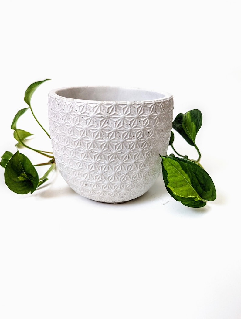 Op de afbeelding: Witte keramische pot met een geometrisch patroon. De pot is leeg en heeft een afgeronde vorm.