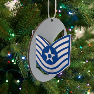 Peut inclure: Une décoration de Noël bleue et argentée en forme d'insigne de grade de sergent technique de l'armée de l'air. La décoration est suspendue à un sapin de Noël vert.
