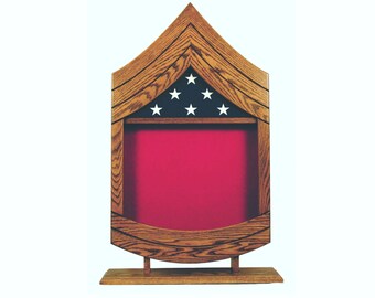 May include: A wooden shadow box with a red felt interior and a blue and white star design on the top. The shadow box is shaped like a chevron and is on a wooden base.