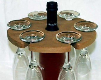 May include: A wooden wine bottle and glass holder with six slots for glasses. The holder is made of light brown wood and has a dark red wine bottle in the centre. The glasses are clear and are hanging upside down from the holder.