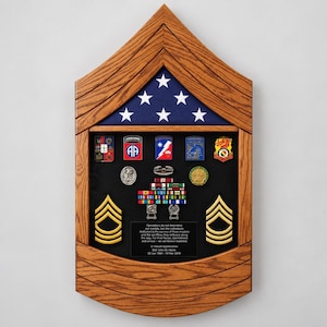May include: A wooden shadow box shaped like a military chevron, featuring a folded American flag at the top and a black display area containing various military medals, pins, ribbons, and two gold chevron patches with an engraved plaque.