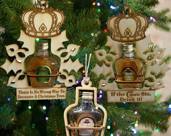 May include: Three wooden Christmas decorations featuring a crown design and a miniature bottle of Crown Royal whisky. The decorations have the text "There Is No Wrong Way To Decorate A Christmas Tree." and "If the Crown fits, Drink it!"