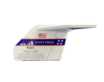 May include: A white, airplane-shaped commemorative item with blue and red details. It features the text "SCOTT FIELD", a US flag, and the number "40125". Additional text includes a quote and dates.