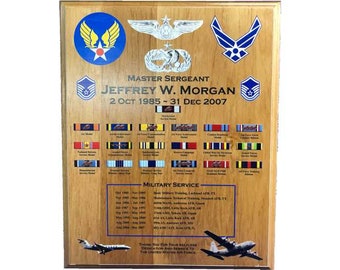 May include: A wooden plaque with a blue, white, and red Air Force emblem, a silver pilot's wings, and a Master Sergeant rank insignia. The plaque is inscribed with the name "JEFFREY W. MORGAN", the dates "2 OCT 1985 - 31 DEC 2007", and the text "MILITARY SERVICE". The plaque also features a list of military awards and decorations, and a small image of an airplane.