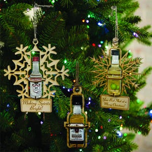 May include: Three wooden Christmas decorations shaped like snowflakes, each with a miniature liquor bottle inside. The decorations are decorated with the text "Making Spirits Bright!" "Your Best Shot at a Merry Christmas!" and "Evan Apple".