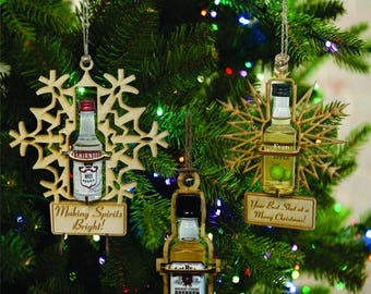 May include: Three wooden Christmas decorations shaped like snowflakes, each with a miniature liquor bottle inside. The decorations are decorated with the text "Making Spirits Bright!" "Your Best Shot at a Merry Christmas!" and "Evan Apple".