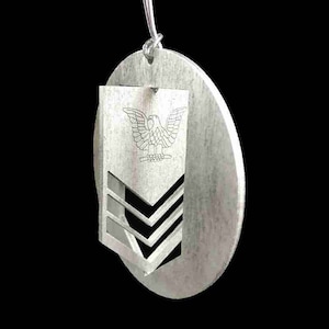 May include: Silver ornament with a silver eagle and three chevrons, representing a military rank.