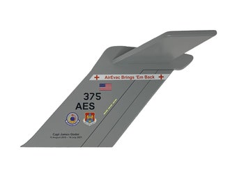 May include: A grey aircraft tail with the words "AirEvac Brings 'Em Back" and the number "375 AES" printed on it. The tail also has a red cross, an American flag, and a few other insignia.