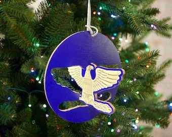 May include: A blue and gold Christmas bauble featuring a stylised eagle with outstretched wings. The bauble is hanging on a Christmas tree.