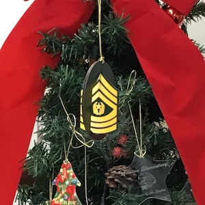 Puede incluir: Un árbol de Navidad decorado con adornos, incluyendo un adorno de madera con forma de insignia de rango militar, un adorno rojo y verde con la palabra "Merry" y un adorno de vidrio transparente con el texto "Ariton Elementary, Home of the Eagles".
