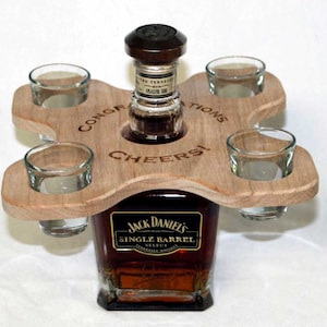 May include: Wooden shot glass holder with four shot glasses and a bottle of Jack Daniel's Single Barrel Tennessee Whiskey. The holder has the words "Congratulations" and "Cheers!" engraved on it.