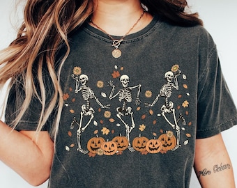 Op de afbeelding: Donkergrijs t-shirt met een Halloween-ontwerp. De afbeelding toont drie dansende skeletten met zonnebloemen, pompoenen en herfstbladeren. Het shirt is een comfortabele, casual stijl.