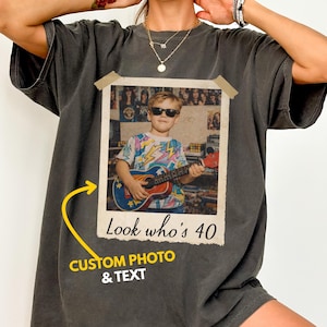 Puede incluir: Camiseta gris oscuro con una foto de estilo vintage y el texto "Look who's 40". La foto muestra a una persona con gafas de sol tocando la guitarra. La camiseta tambi&eacute;n tiene el texto "CUSTOM PHOTO & TEXT".