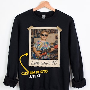 Puede incluir: Sudadera negra con foto y texto personalizados. La foto muestra a una persona con gafas de sol tocando la guitarra. El texto de la foto dice "Look who's 40". La sudadera tambi&eacute;n tiene el texto "CUSTOM PHOTO & TEXT".