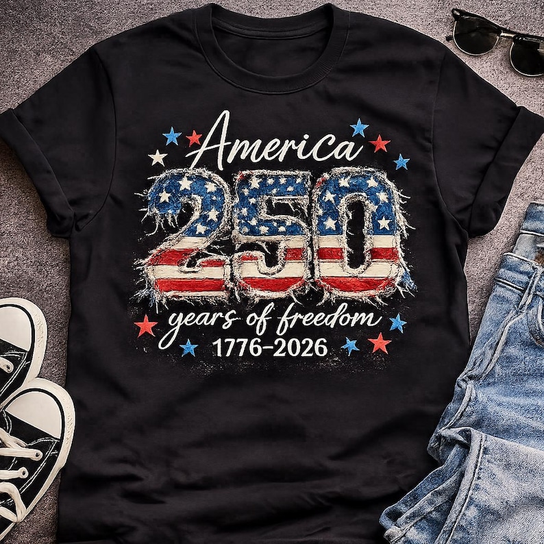 May include: Black t-shirt with the text "America 250" in a patriotic design. The number 250 is styled with a blue stars and stripes pattern, with the words "years of freedom 1776-2026" below.