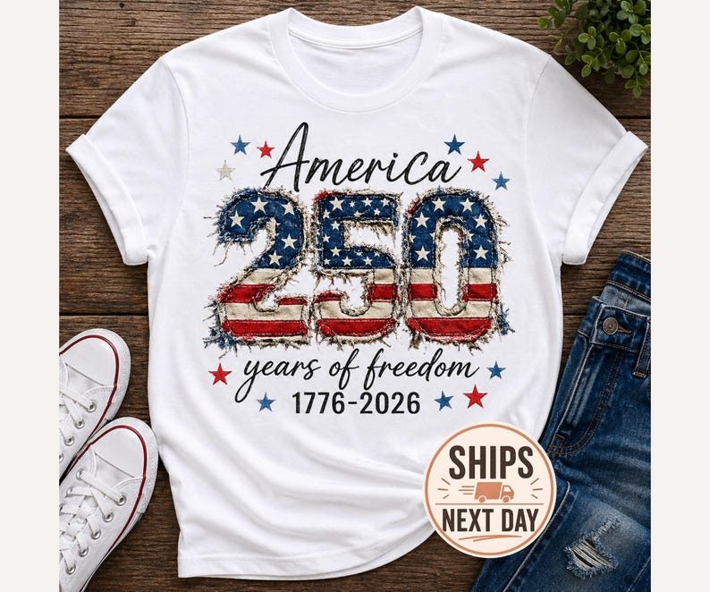 May include: White t-shirt with the text "America 250 years of freedom 1776-2026" in black script. The number "250" is designed with a distressed American flag pattern. Red and blue stars surround the text.