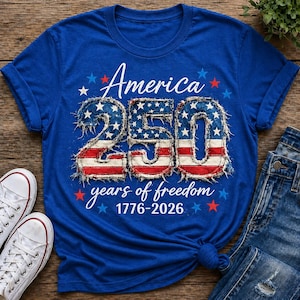 May include: A blue t-shirt with the text "America 250 years of freedom 1776-2026" in white script and a patriotic design. The numbers "250" are in red, white, and blue, with a distressed flag pattern.