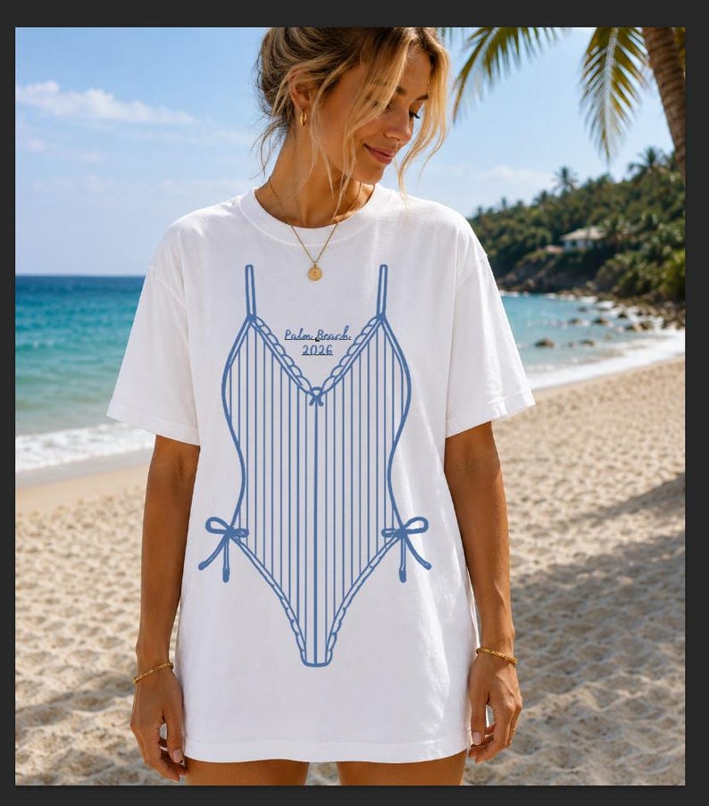 May include: White t-shirt featuring a blue swimsuit design with vertical stripes, bows, and the text "Palm Beach 2026." The shirt is worn on a beach with a blue ocean and palm trees in the background.