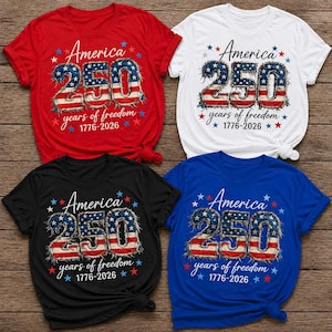 May include: Four short-sleeved t-shirts in red, white, black, and blue. Each shirt features the text "America 250 years of freedom 1776-2026" in a patriotic design with stars and the American flag colors.