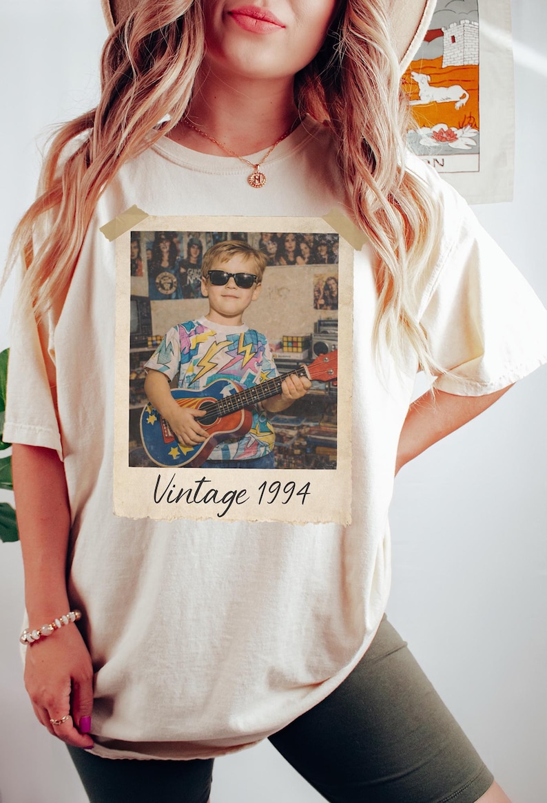 Puede incluir: Camiseta color crema con estampado de foto vintage. La foto muestra a una persona con gafas de sol tocando un ukelele. La foto lleva la leyenda "Vintage 1994".